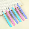 A set of five colored craft tweezers with pink, blue, and purple handles resting on a grid paper background.