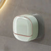 A round, light green wall mounted soap dish with a pink trim is mounted on a neutral gray wall.