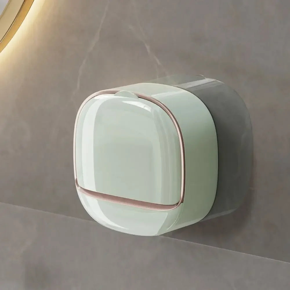 A round, light green wall mounted soap dish with a pink trim is mounted on a neutral gray wall.