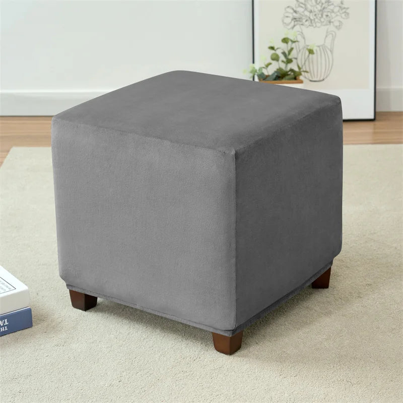 A square gray stretch velvet ottoman slipcover resting on a light carpet.