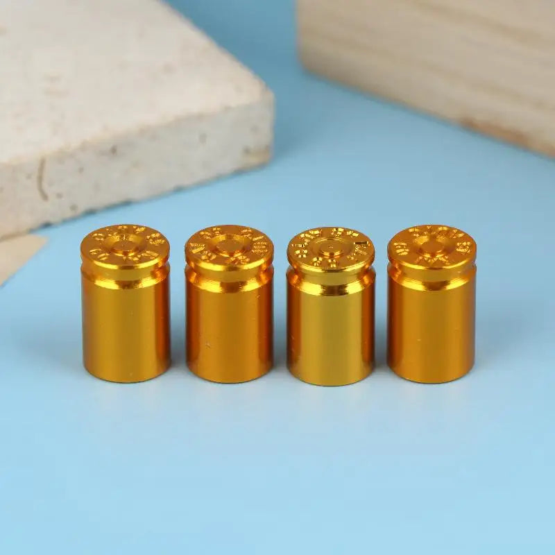 A set of four gold-colored bullet shell tire valve stem caps resting on a light blue surface.