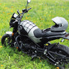 A black and silver motorcycle is parked on green grass, featuring a bungee cargo net system.