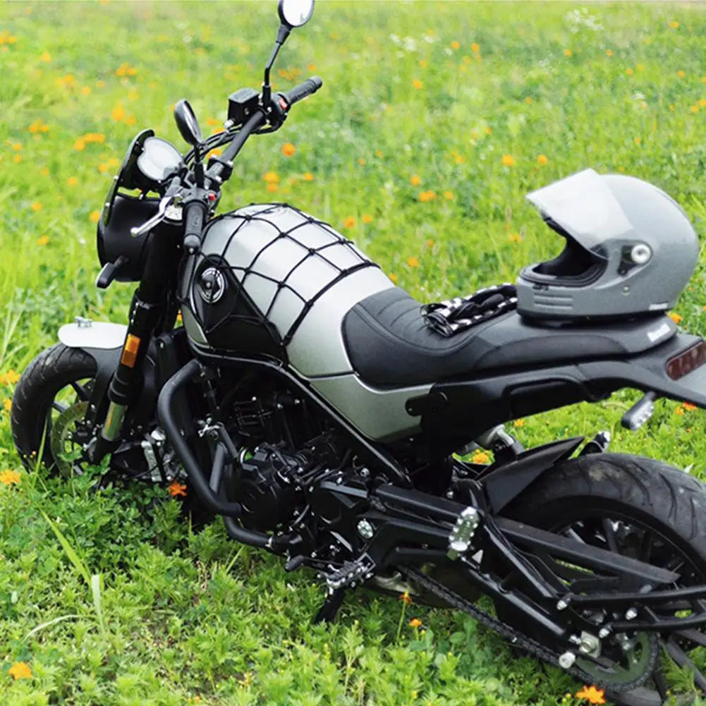 A black and silver motorcycle is parked on green grass, featuring a bungee cargo net system.