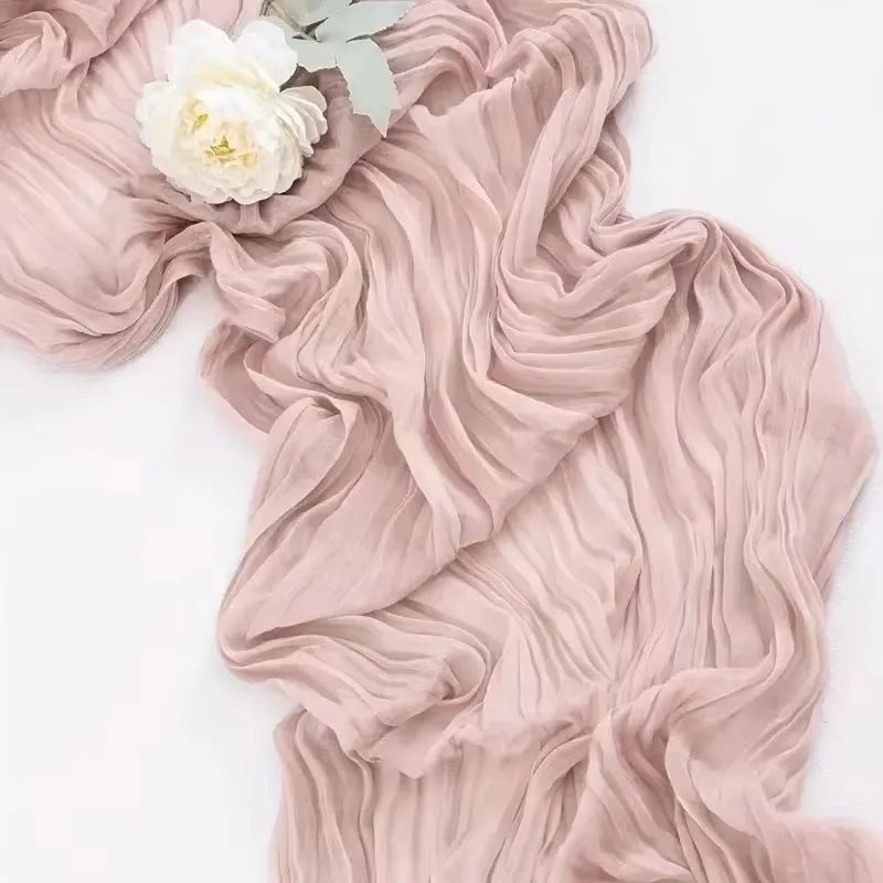 A flowing, dusty rose cotton gauze table runner with soft pleats and a white flower detail.