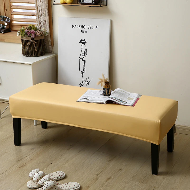 A yellow waterproof PU stretch bench cover is placed on a wooden floor next to a framed art print.