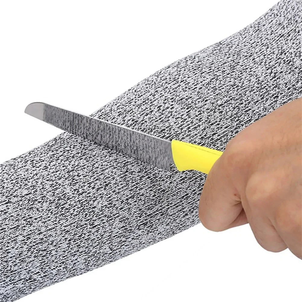 A hand holds a knife inserted into a gray and black textured arm sleeve for industrial safety.