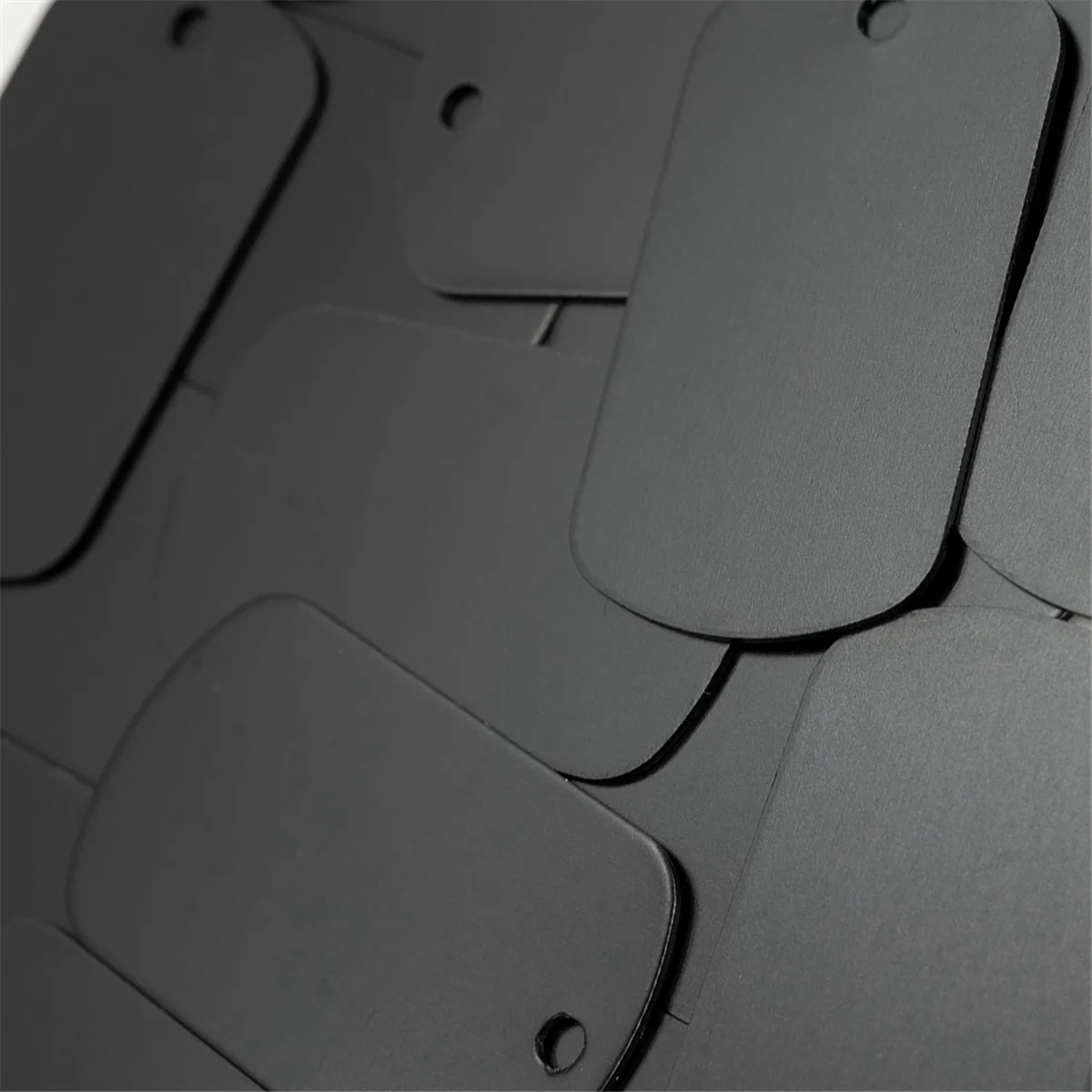 A close-up view of a stack of black aluminum stamping blanks for DIY engraving dog tags.