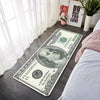 A US dollar banknote lying on a gray floor mat next to a white window and a pink plant.