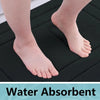 A close-up of a foot resting on a black absorbent bath mat, showing skin texture and water absorption.