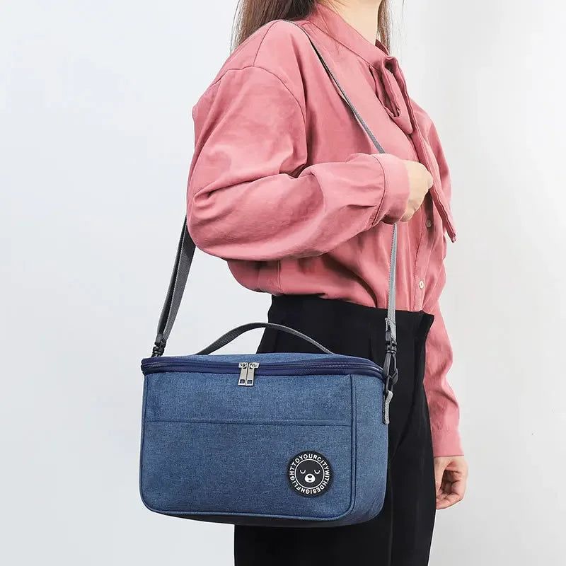 A woman holds a navy blue insulated lunch bag with a shoulder strap against a white background.