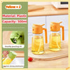 An orange plastic oil spray bottle with a green top is shown pouring yellow oil onto a wooden cutting board.