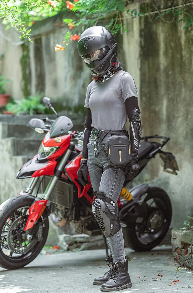 A person wearing a black motorcycle helmet and black gloves stands next to a red motorcycle with a black hip pack.
