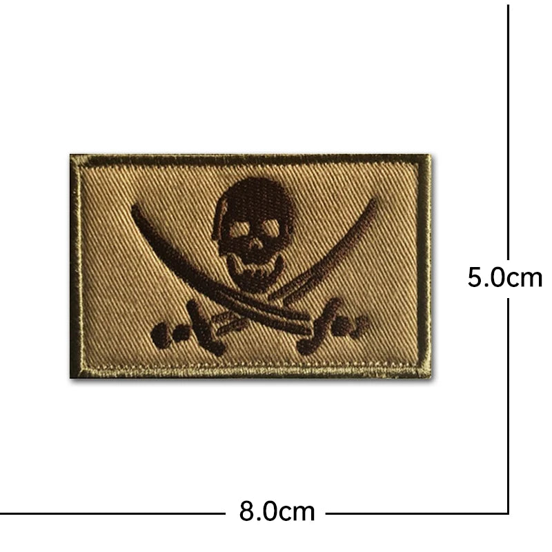 A rectangular gold embroidered patch featuring a skull and crossed swords design.
