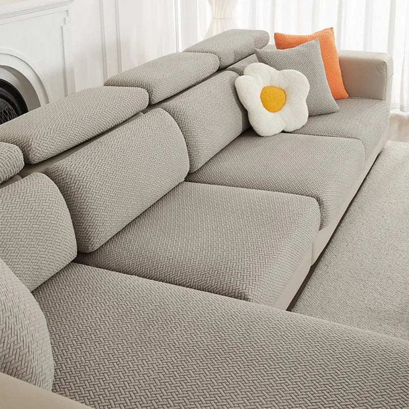 A light gray jacquard elastic sofa slipcover with orange accent pillows on a white background.