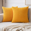 A bright yellow textured corduroy throw pillow resting on a light-colored sofa with a white knitted blanket.