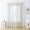 Sheer white voile curtains hanging in a window with a light wood table and chair nearby.