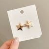 A pair of gold-toned star-shaped metal brooches displayed on a white card.