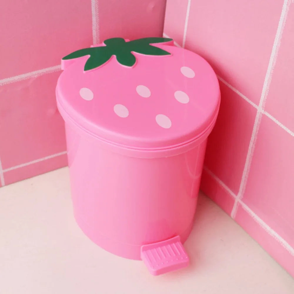 A pink mini strawberry trash can with a green pop-up lid sitting on a white surface.