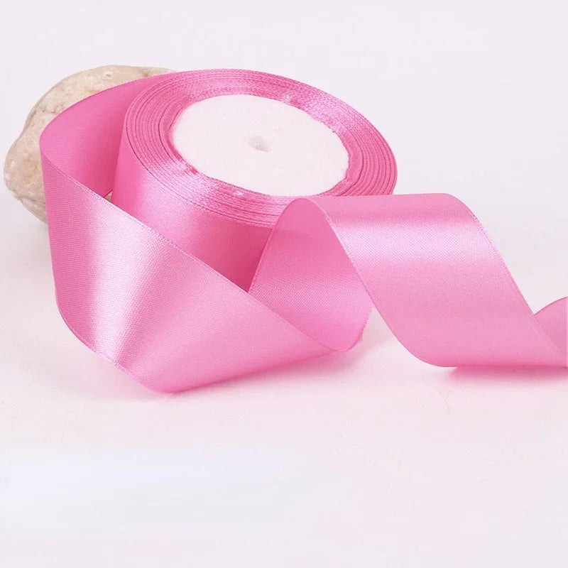 A roll of pink satin ribbon for gift wrapping and crafts, shown against a white background.