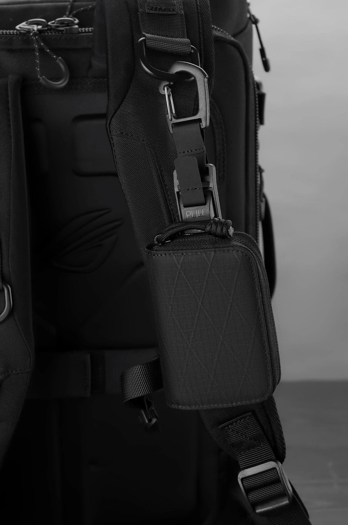 A close-up view of a black RFID wallet attached to a dark backpack strap.
