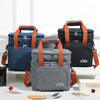 A gray insulated lunch bag with orange straps is displayed next to a dark blue one on a white surface.