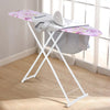 A white foldable ironing board with a purple floral cover is shown next to a window.