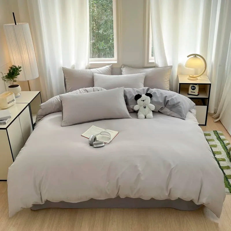 A light gray quilted duvet cover set with matching pillowcases on a bed in a bright, softly lit room.
