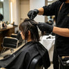 A hairstylist wearing black gloves is styling a client's hair in a salon setting.