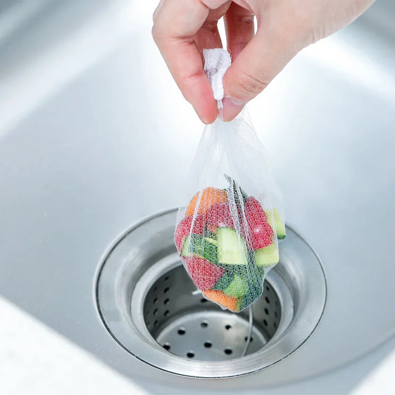 A hand is placing a mesh bag filled with colorful vegetable scraps into a metal sink drain filter.