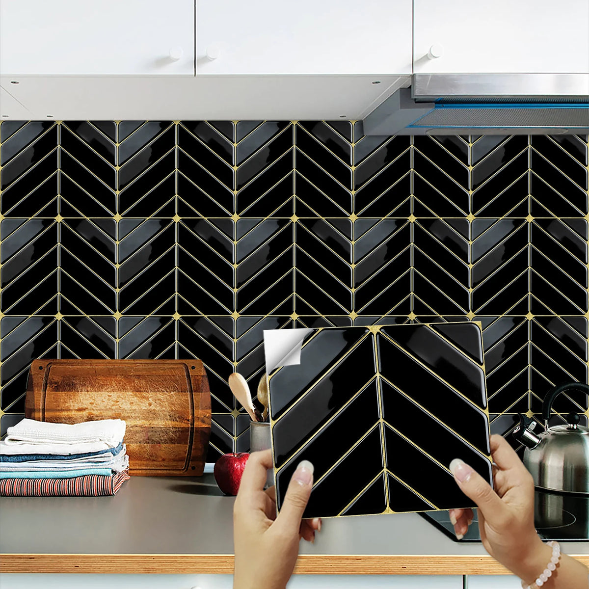 Hands holding a black marble peel-and-stick tile pattern against a dark tiled backsplash.