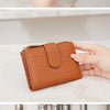 A close-up of a brown crocodile-embossed PU leather bifold wallet with a gold accent, shown being held by a hand.