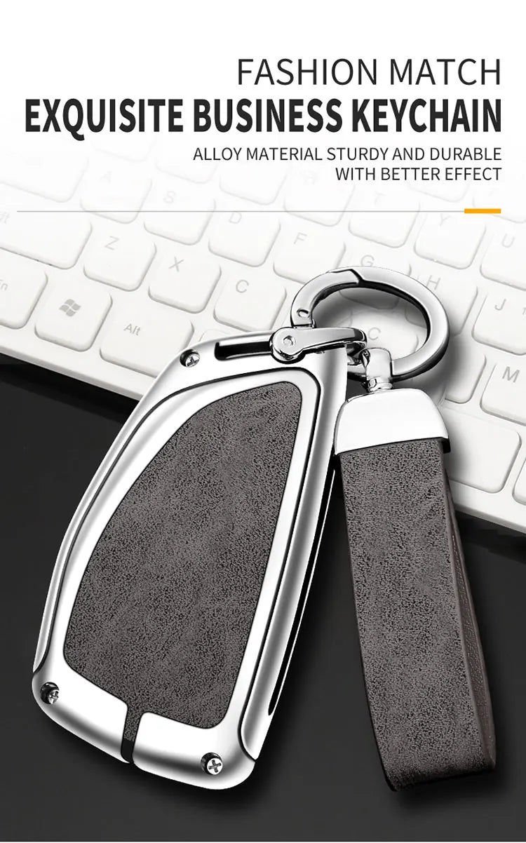 A silver key chain with a leather strap and metal clasp resting on a white computer keyboard.