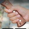 A hand holds a solid wood handle of a splitting axe, showing the grip and rivets for structural stability.