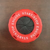 Red circular cover with text START/STOP ENGINE and a black rotating button for an engine start function