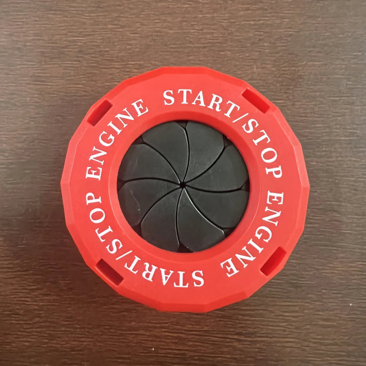 Red circular cover with text START/STOP ENGINE and a black rotating button for an engine start function