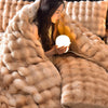 A woman is wrapped in a fluffy beige faux fur blanket while holding a glowing light source.