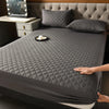 A dark gray quilted waterproof mattress protector is shown on a bed with matching pillows and a small tray.