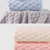 A stack of four plush bath towels in shades of pink, white, blue, and gray.
