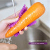 Une main utilise une carotte orange pour nettoyer une surface avec une brosse à légumes en silicone violet.