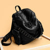 A black soft leather backpack with silver rivets is shown on a light background.