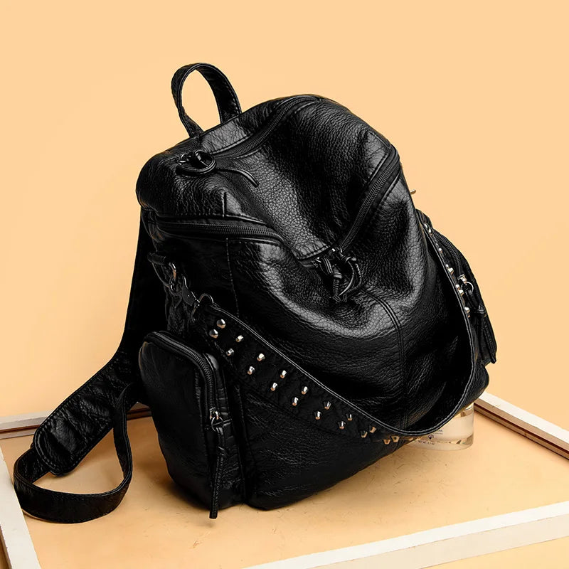 A black soft leather backpack with silver rivets is shown on a light background.