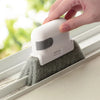 A hand is using a white multi-surface gap cleaning brush with a scouring pad to clean a window sill.