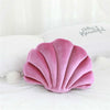 A pink velvet shell print decorative throw pillow resting on white bedding.