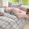 A pink and blue plaid duvet cover set with two pillows and a pair of light blue headphones on a bed.