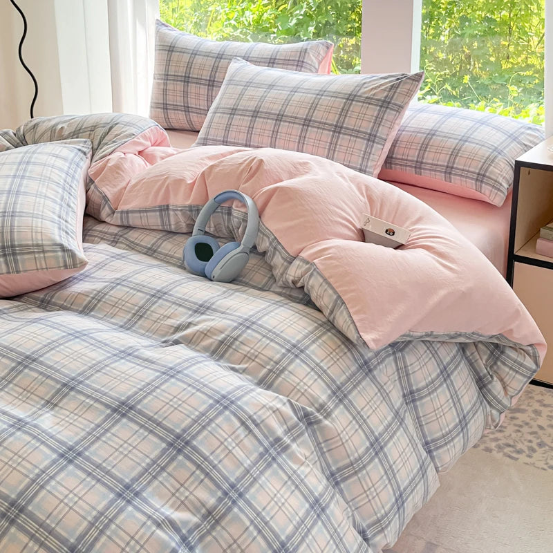 A pink and blue plaid duvet cover set with two pillows and a pair of light blue headphones on a bed.