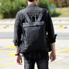 Person in black denim jacket and dark pants carrying a black genuine cowhide leather backpack.