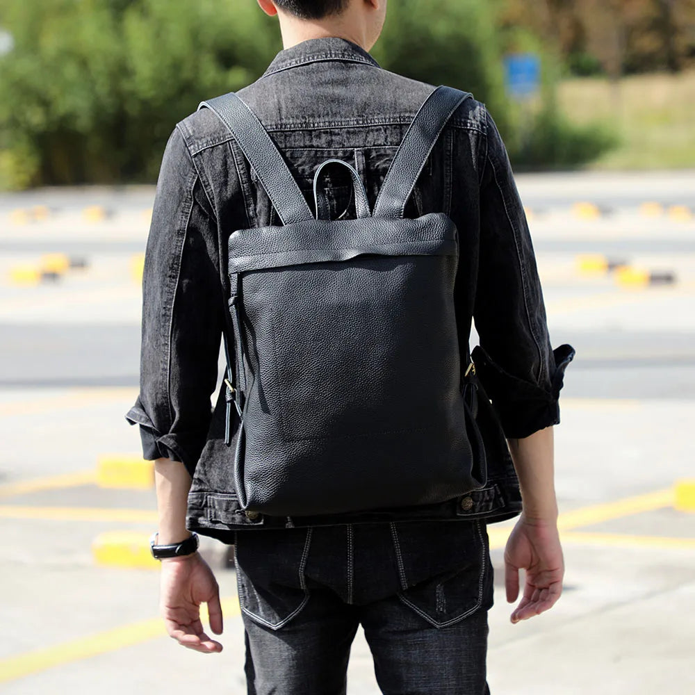 Person in black denim jacket and dark pants carrying a black genuine cowhide leather backpack.