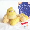 A yellow crocheted duck toy next to yarn and a purple DIY crochet kit bag.