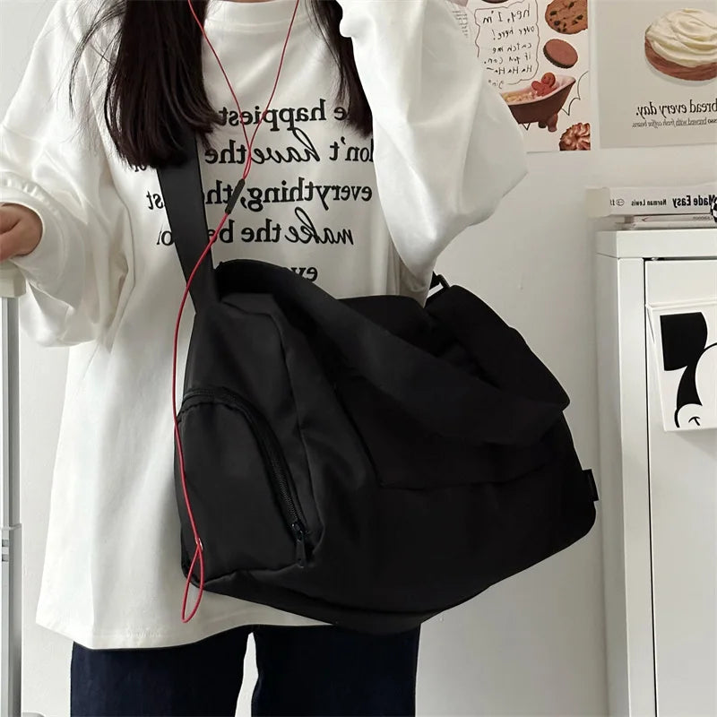 A black large canvas travel tote bag with a red crossbody strap is shown being held by a person in a white shirt.