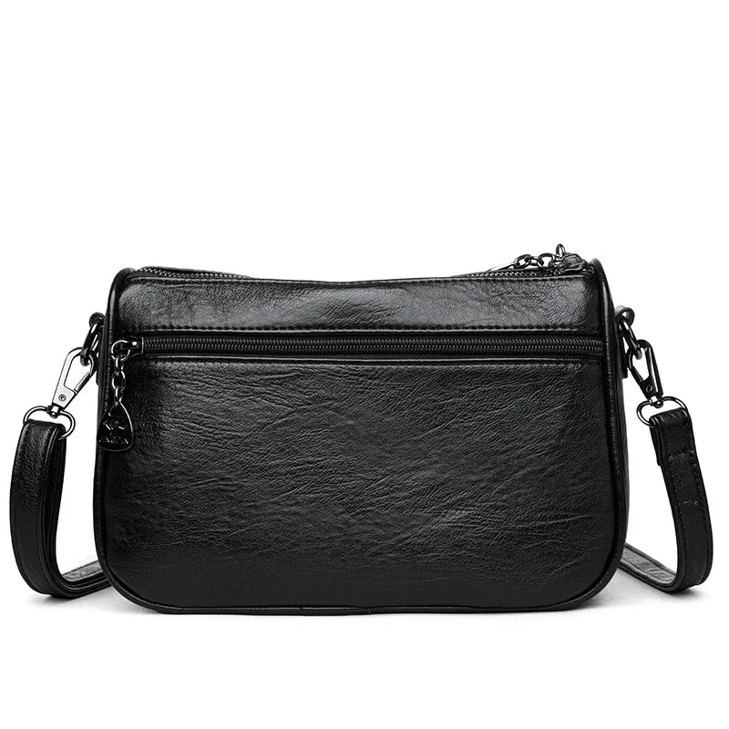 Black leather compact square crossbody bag with a zippered top and a chain strap.